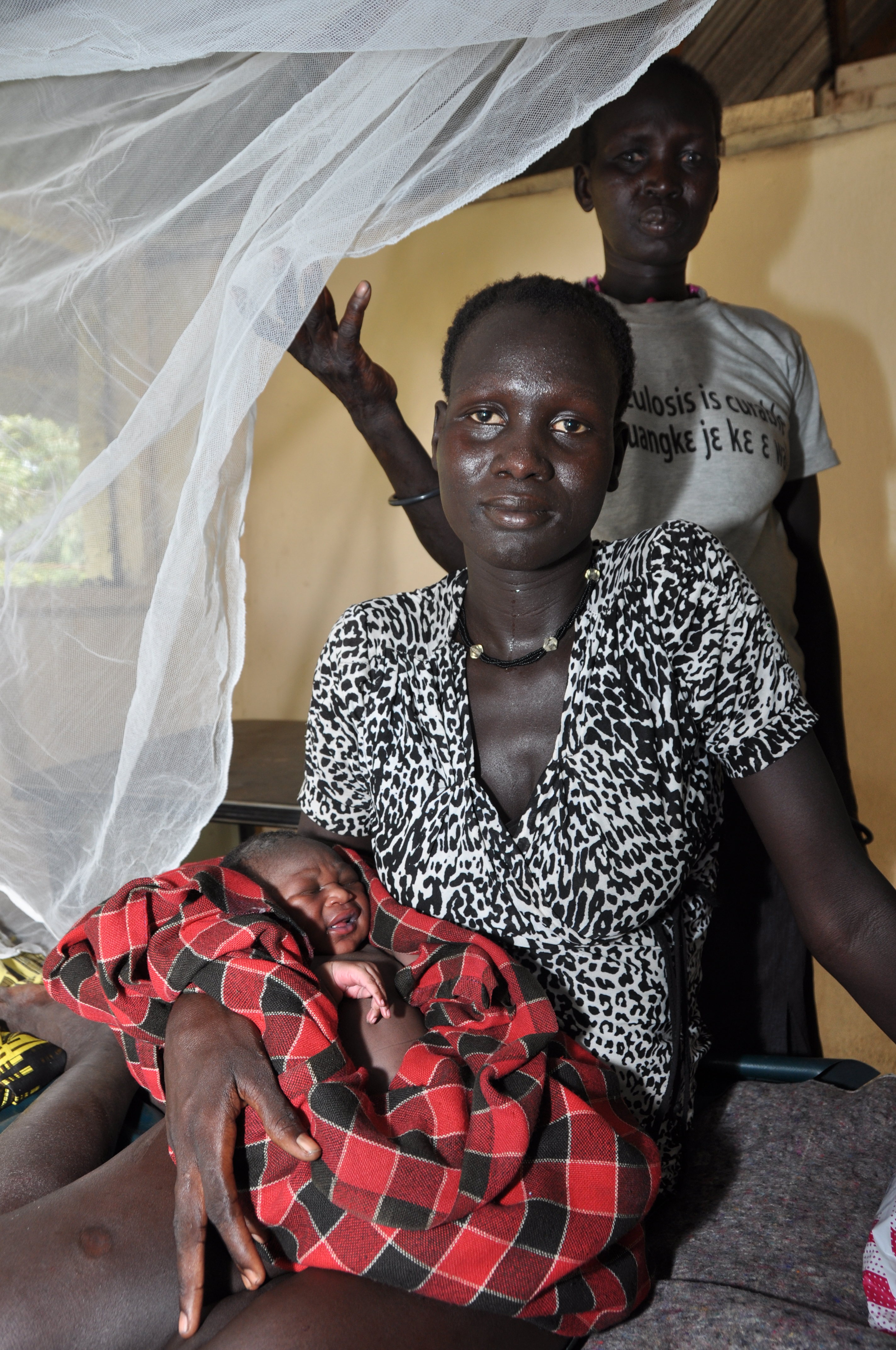 A mother holds her newborn in her arms, exhausted but happy. The traditional birth attendant in the background helped her deliver at the bush clinic run by Sign of Hope in Nyal, South Sudan. A mother holds her newborn in her arms, exhausted but happy. The traditional birth attendant in the background helped her deliver at the bush clinic run by Sign of Hope in Nyal, South Sudan.